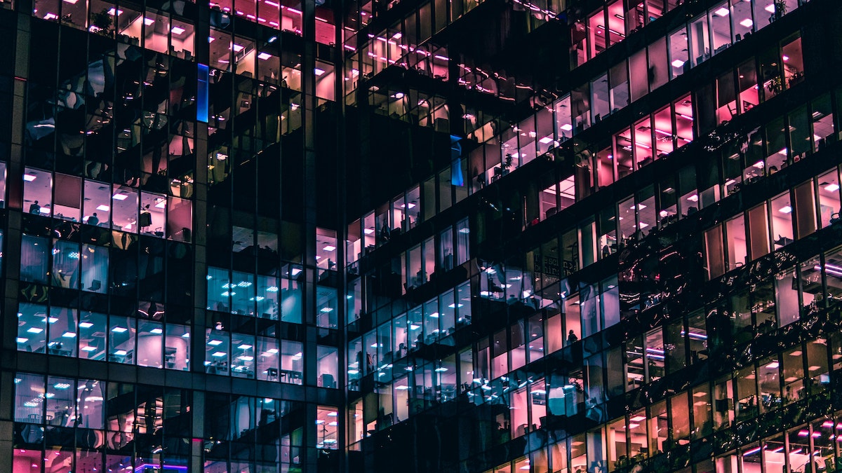 Glass skyscraper with rose and blue lights shining out from the offices.